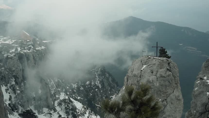 Cross standing high on a rocky top as low clouds hover near