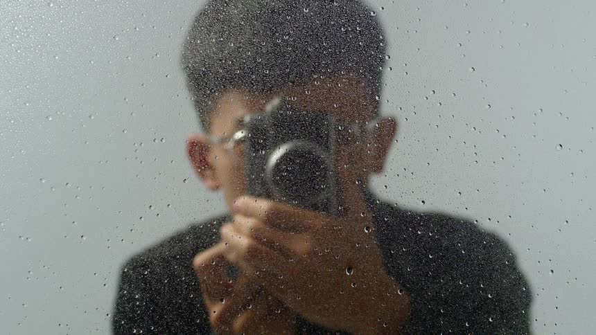 A young man photographs a wet sheet of glass