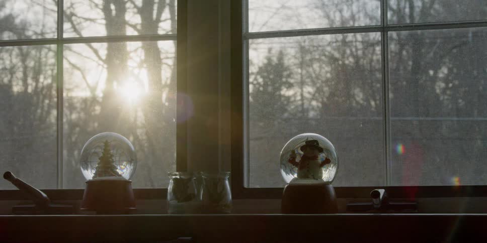 The sun is shining through a window onto two snow globes during the day