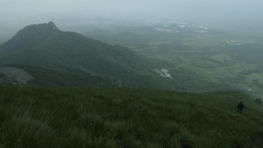 A man climbs up a grassy hill under overcast skies