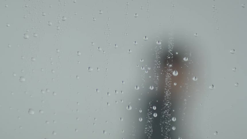 Water droplets on glass and the shadow of a person moves behind it