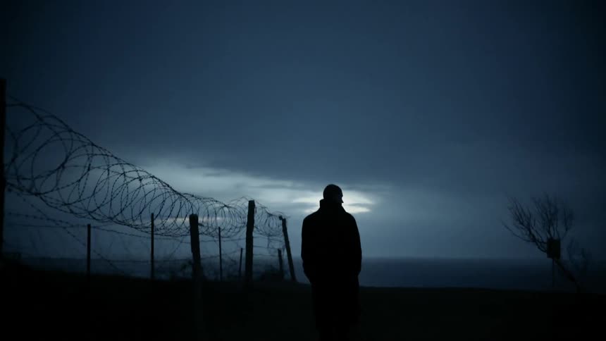 A man walks next to a rural barbed wire fence at night