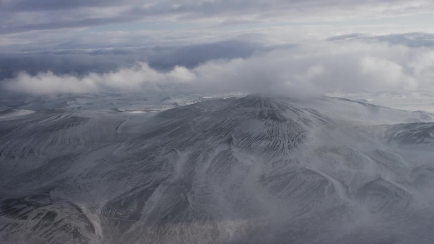 Aerial view of a snow capped mountain covered in clouds