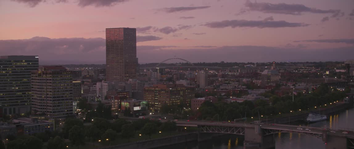 Lights shining out of buildings in a city at sunset