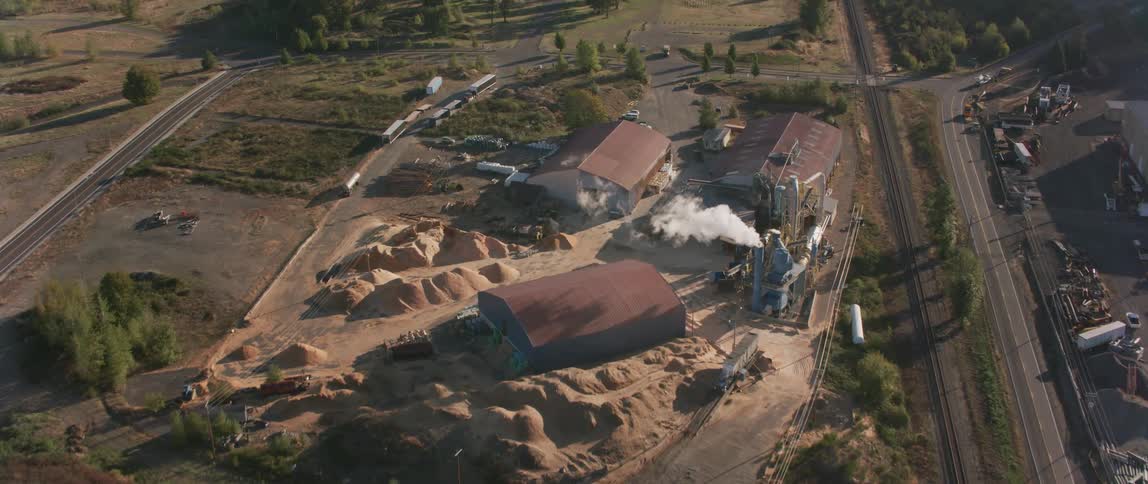 Smoke is pouring from a stack in a factory in a rural setting during the day