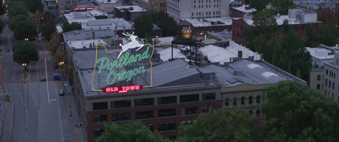 A neon sign advertising portland's old town is flashing above a building at dusk