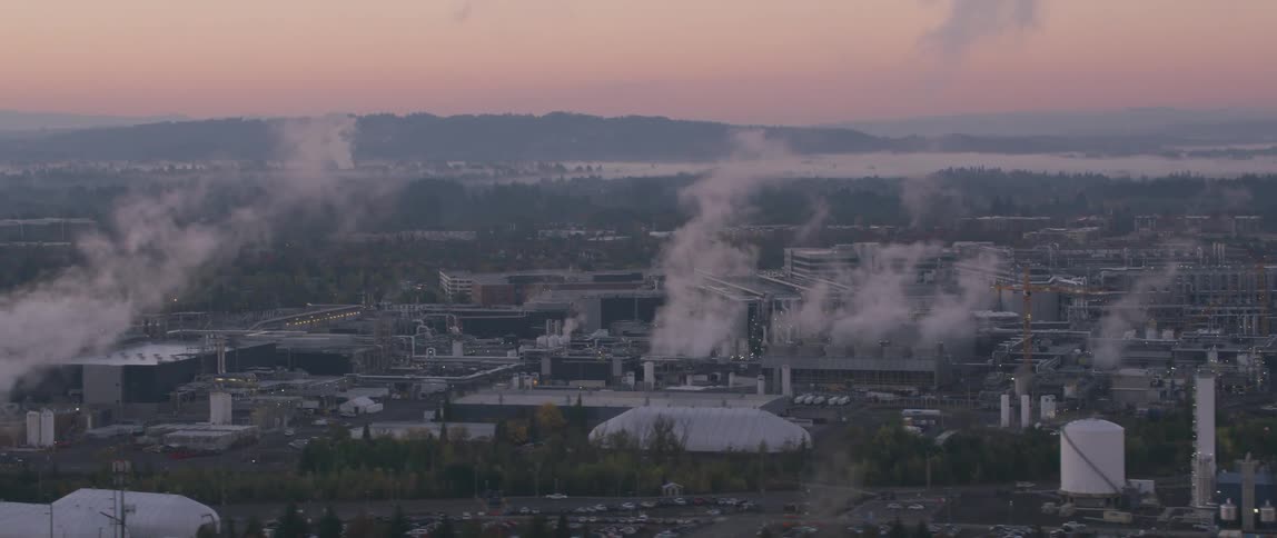 Smoke is rising from stacks in an industrial complex at dusk