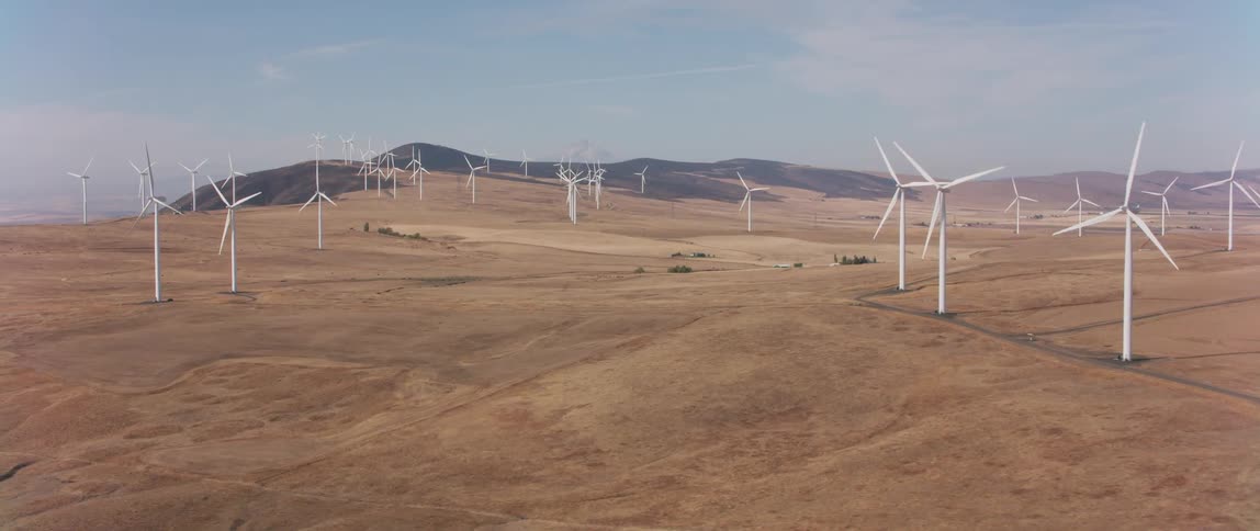 Many tall windmills spread out across the plain are spinning slowly