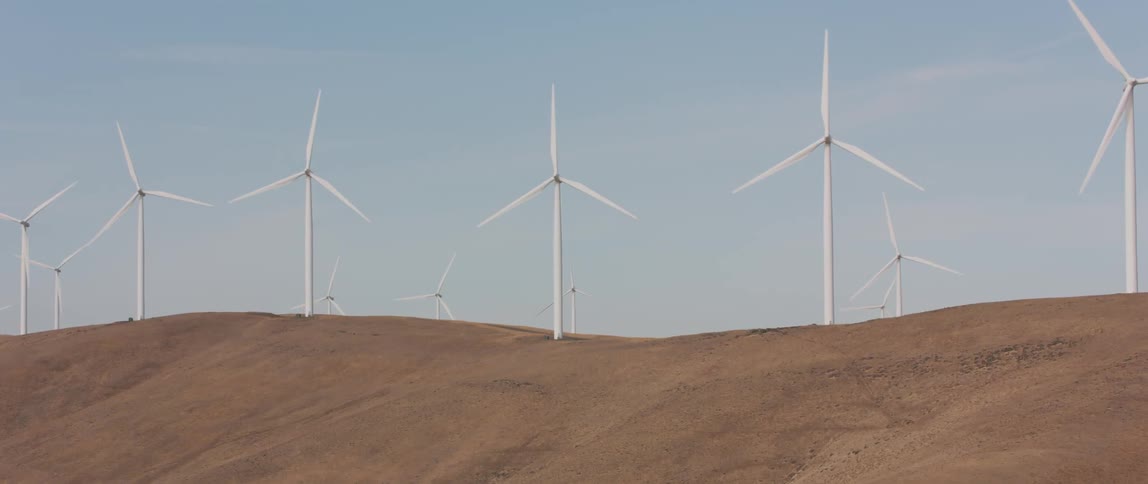 Rows of windmills rotate on hilly dirt land