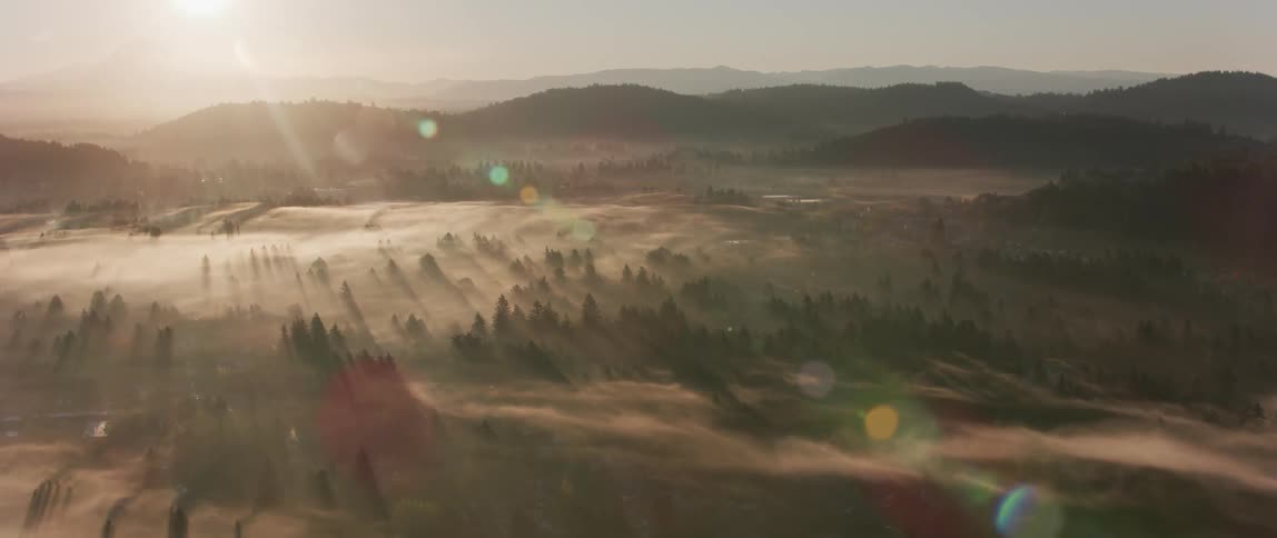 The sun is shining over a vast and open area with trees and mountains