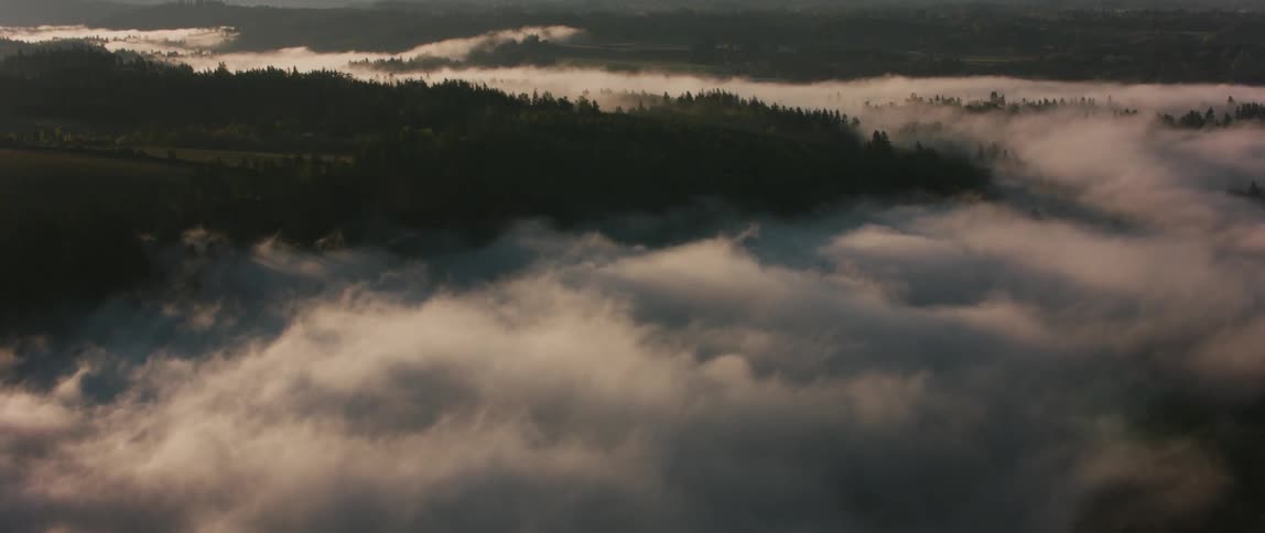 Clouds billow over tree covered hilly land