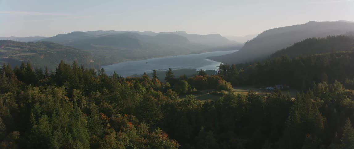 A haze is settling over a lake in a forested mountain setting during the day