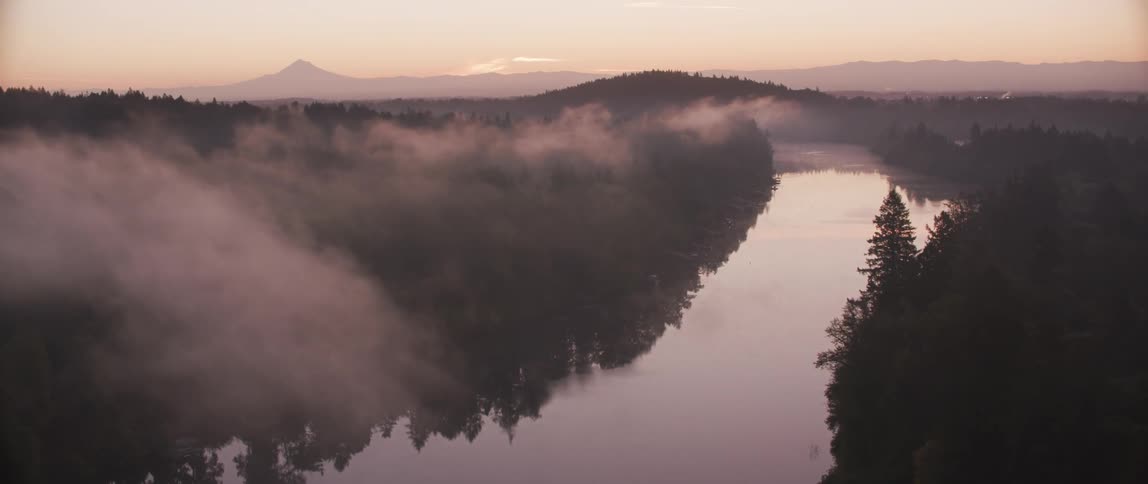 Fog hovers over a river going through the mountains