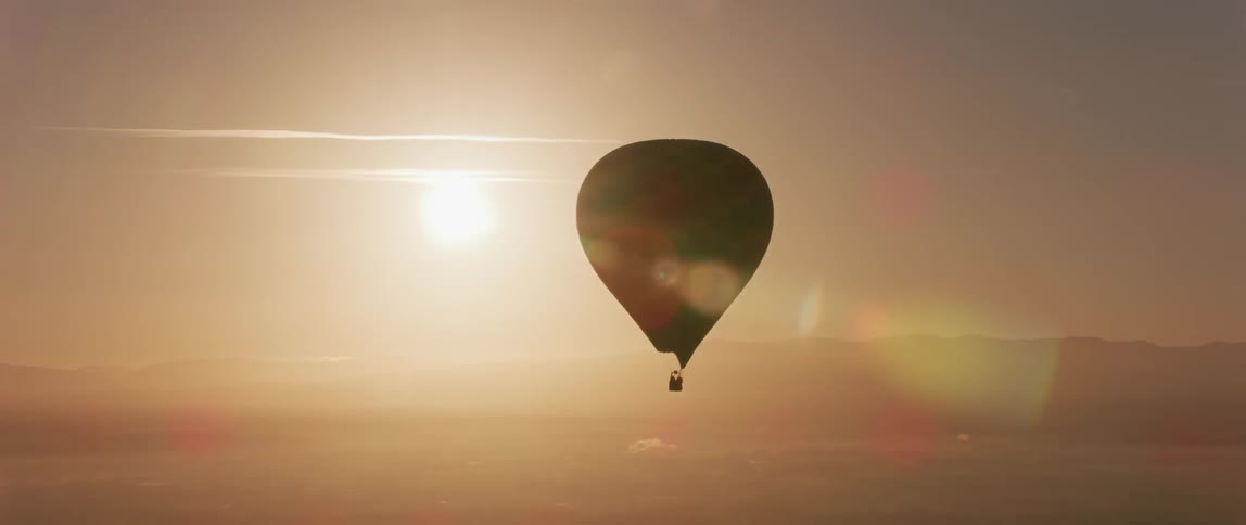 Hot air balloon floating while the sun sets in the distance