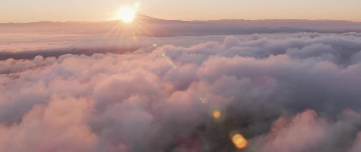 The sun sets over a mountain peak and clouds