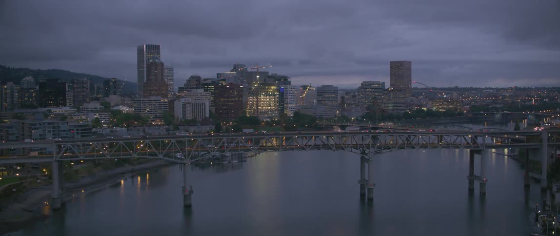 Traffic is crossing a bridge over a river outside a city at dusk