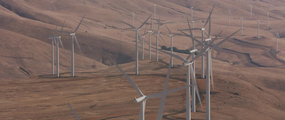 Rows of windmills rotate on hilly dirt land