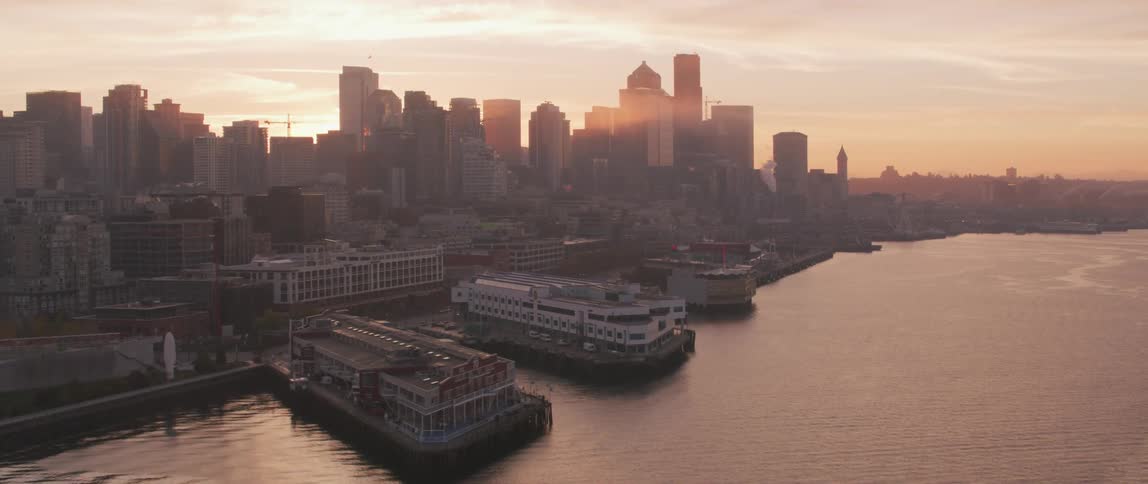 The sun shines on and between tall city buildings by the water
