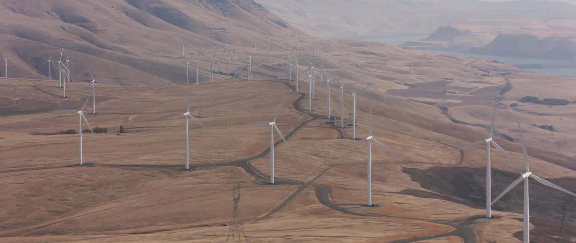 Rows of windmills rotate on hilly dirt land