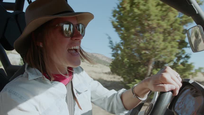 Woman in sunglasses drives a vehicle through a field