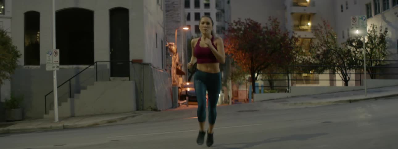 A woman is jogging across a city street at dusk