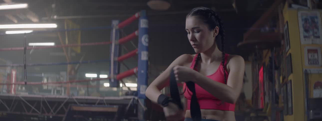 A female fighter is wrapping her hands as she stands outside a boxing ring