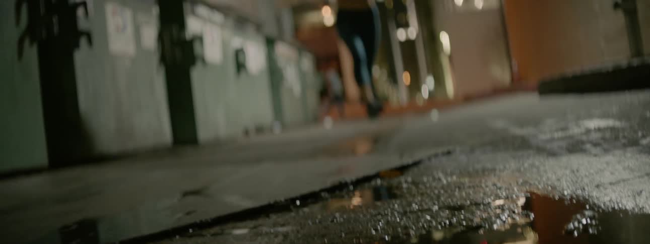 A female jogger is running through a puddle in an urban setting at night