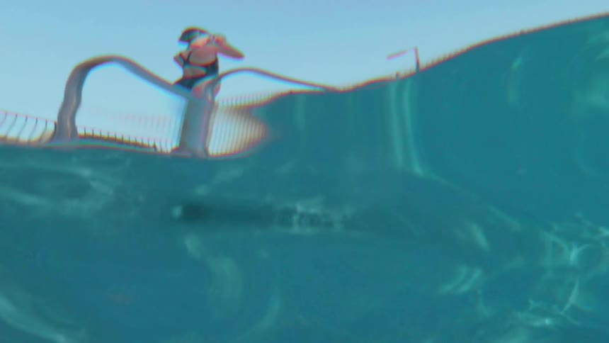 A female swimmer is standing on the edge of a swimming pool in daylight
