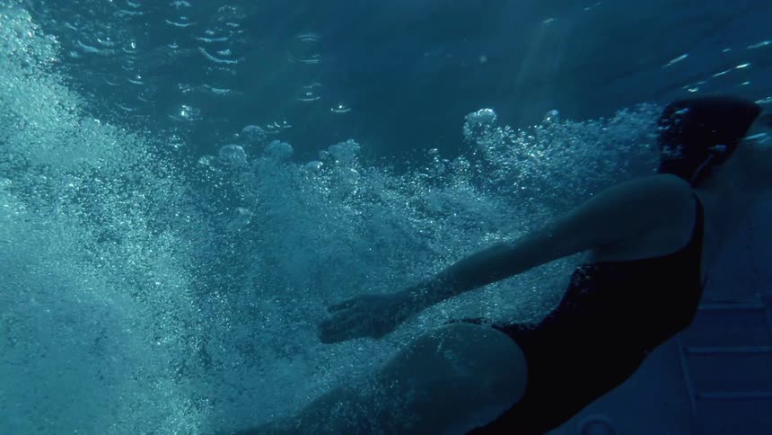 Bubbles are flowing behind a woman as she swims underwater during the day