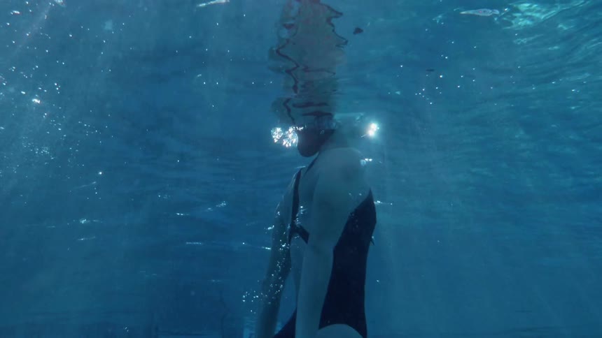 A female swimmer is surfacing from swimming underwater during the day