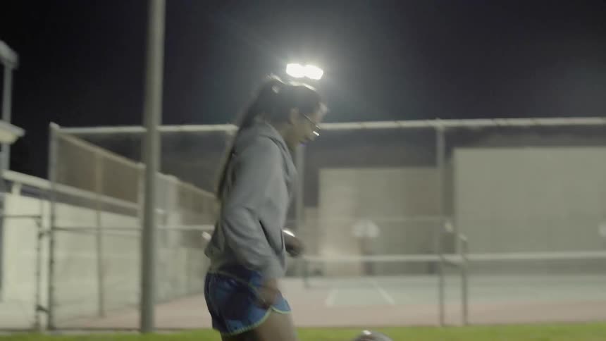 A girl is playing with a soccer ball in a field at night