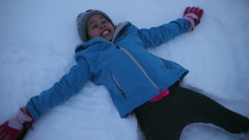 Child making a snow angel and smiling