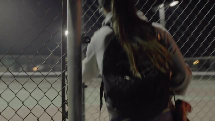 A woman walks into a well-lit fenced area at night