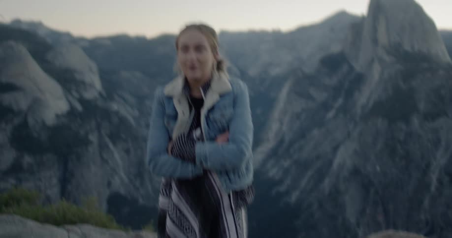 A woman walks on a rock ledge atop a mountain