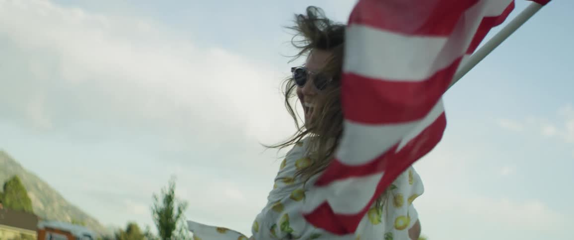 A woman carrying a flag is running and smiling outside in daylight
