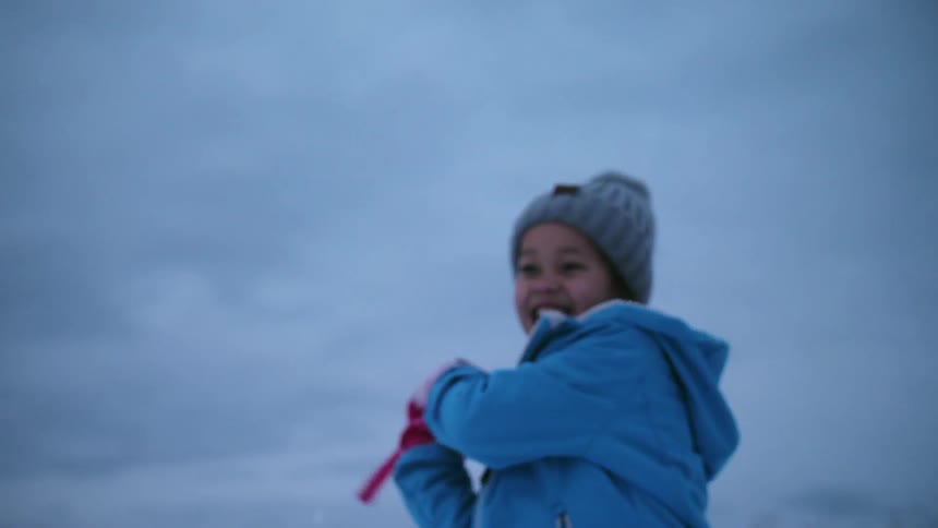 A child is picking up snow and throwing it as he plays outside in winter
