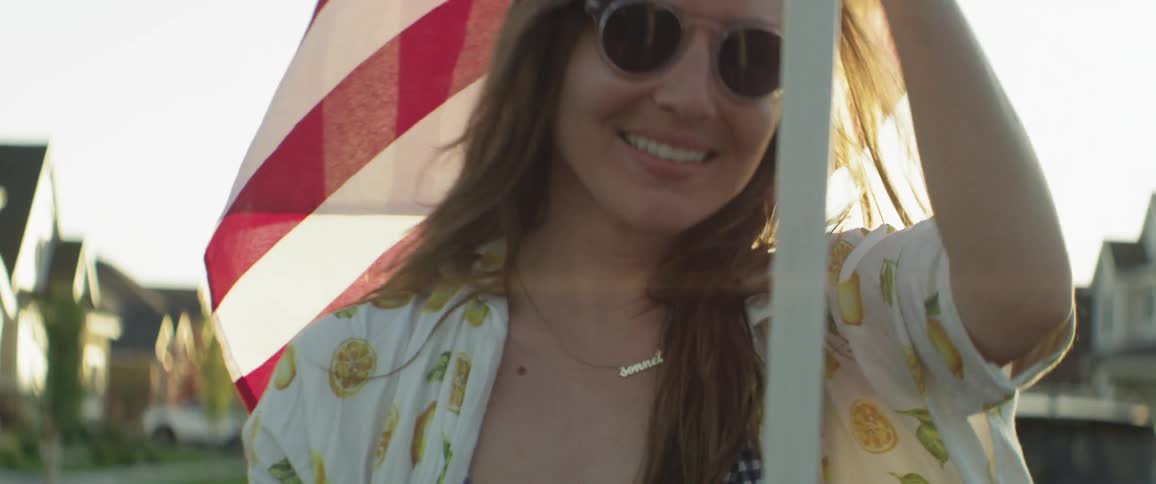 A woman carrying a flag is smiling outside in daylight