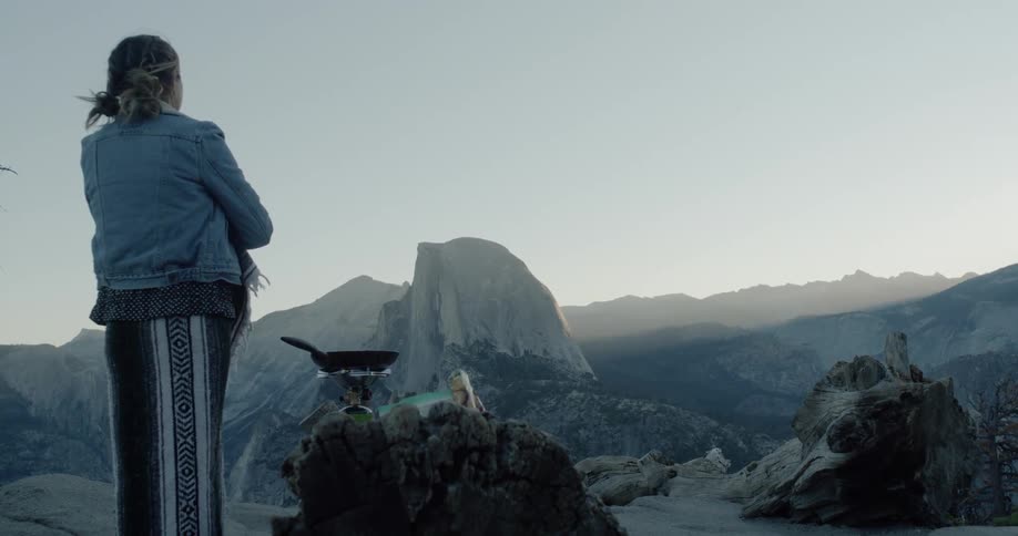 Woman standing in the high wilderness next to a skillet sitting on a makeshift stove