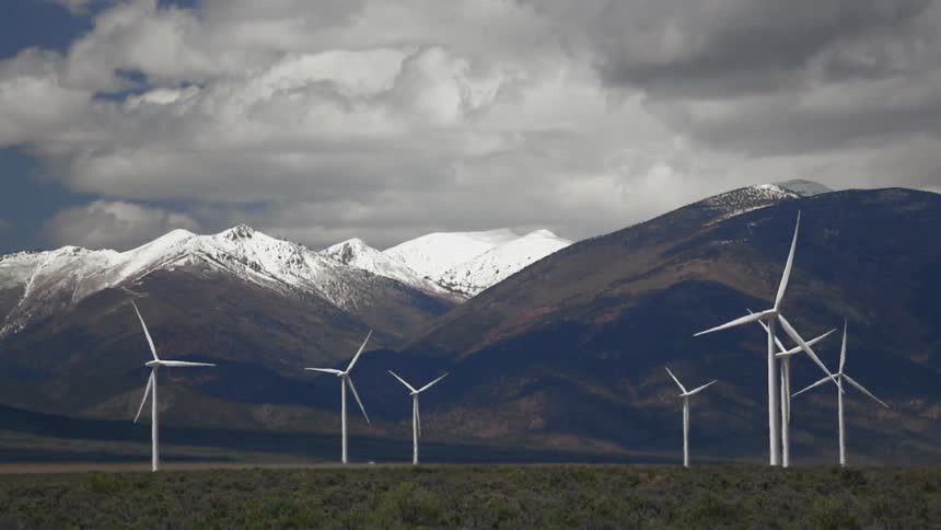 Windmills turning in a field with mountains behind it