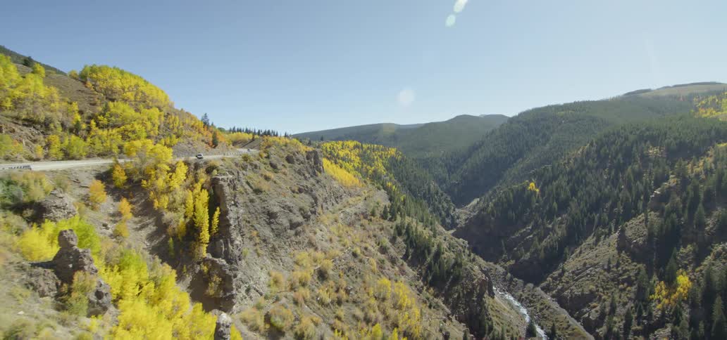 Vehicles are driving on a winding road above a gorge on a sunny day