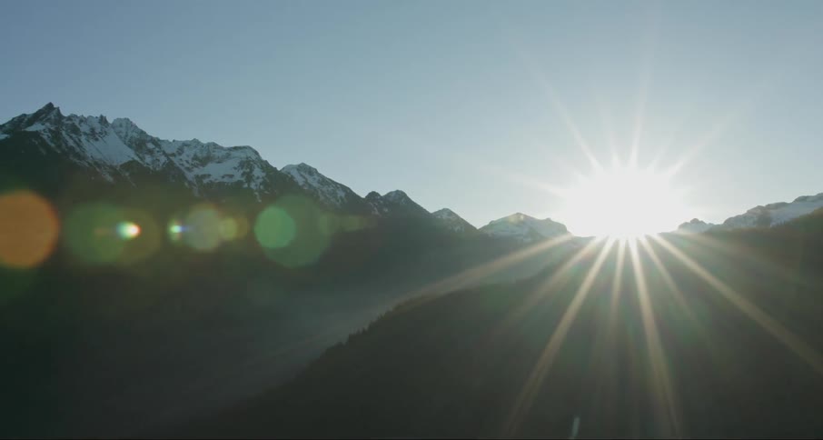 The sun shines over a snowy mountain ridge