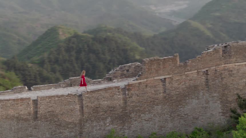 Woman wearing a red dress walks on a tall wall through the mountains