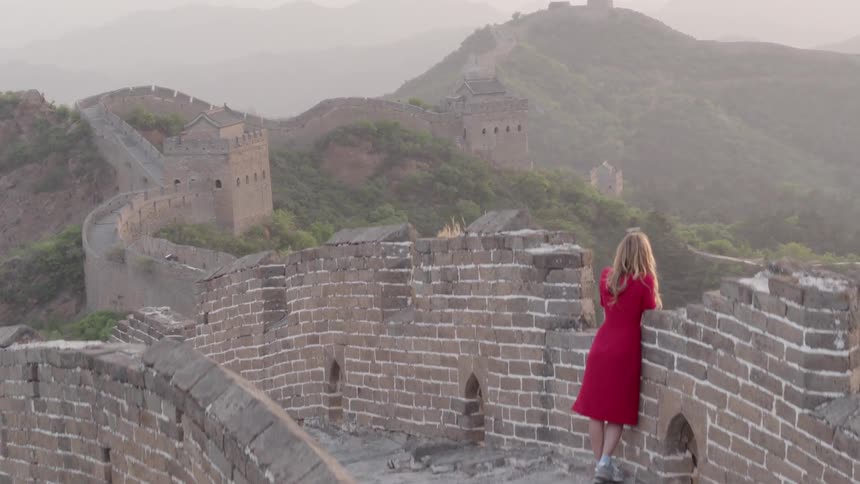 A woman in red watches over a wall lining the hills