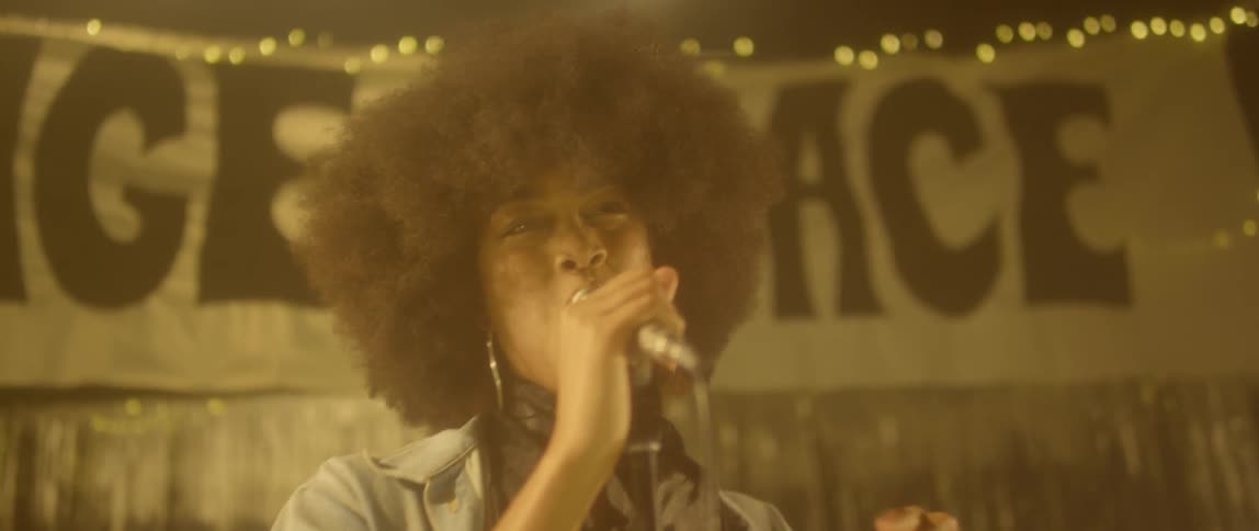 A woman raises her arm and dances while she sings on stage