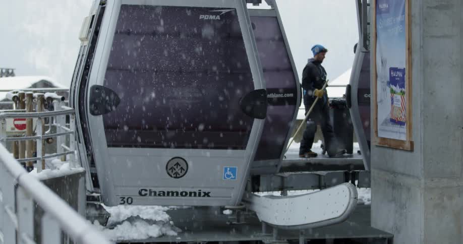 A man is walking near a ski lift as snow is falling