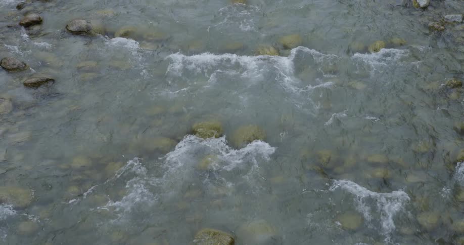 The water splashes against the rocks in the shallow stream