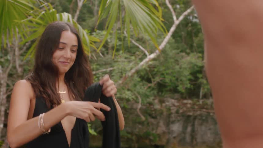 A man removes his shirt as a woman removes her scarf by the woods