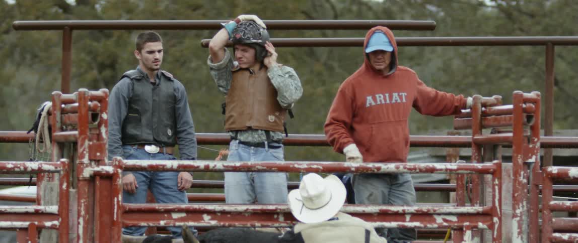 A cowboy is adjusting his helmet as he prepares to ride at a rodeo