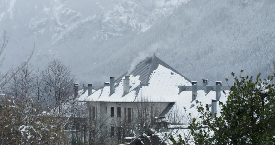 Smoke is rising from the chimney of a building in an alpine setting during the day