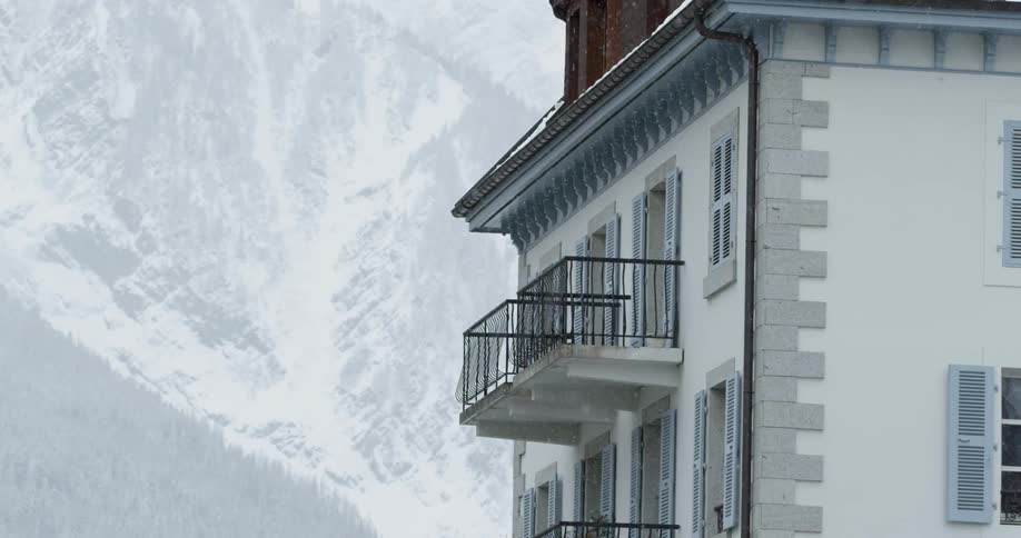 It is snowing by a building near the mountain